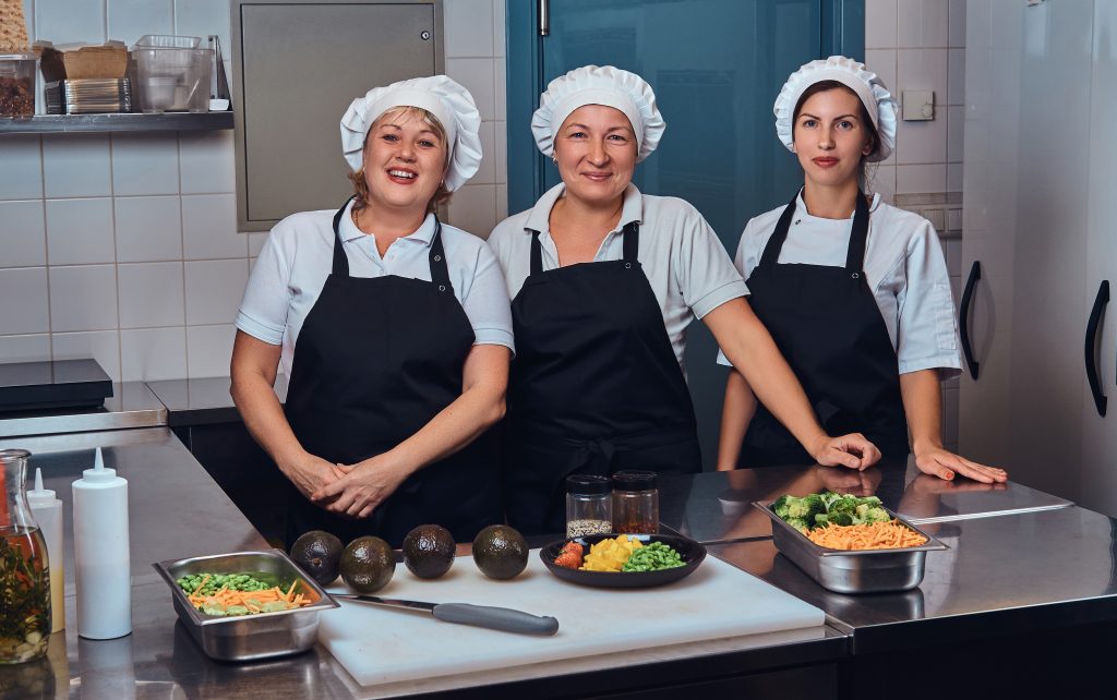 Cooking team standing next to a table with chopped vegetables at restaurant's kitchen